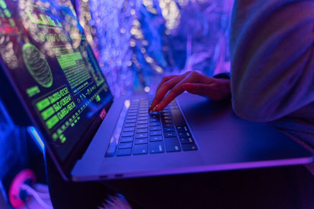 pexels-photo-5475752-5475752 Close-up of hands typing on a laptop displaying cybersecurity graphics, illuminated by purple light.